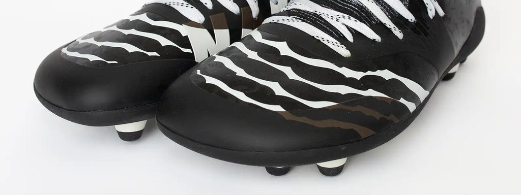 Close-up of Natur adult cleats showing black and white striped design, emphasizing a wide toe box for foot freedom, snug fit heel, and patented cleat plate system for superior traction and comfort. Designed for natural foot mechanics, these cleats provide flexibility, stability, and enhanced performance for athletes