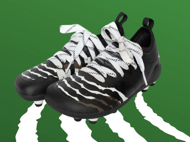 Close-up of Natur cleats featuring a wide toe box and flexible design, set against a green background. These cleats are crafted to respect natural foot mechanics, providing improved stability, comfort, and performance for athletes.