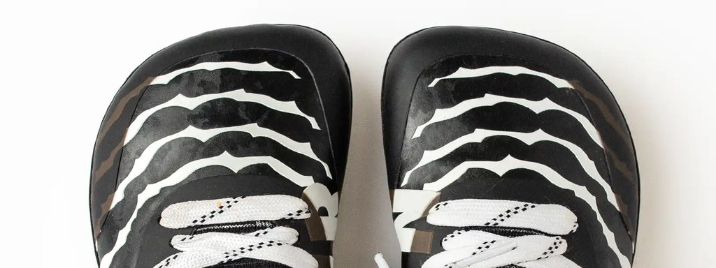 Close-up of Natur Athletics cleats featuring a natural design with a bold black and white striped pattern. The shoes are crafted for optimal comfort, prioritizing natural foot movement and reducing pressure to ensure a comfortable fit for young athletes, helping them focus on their game without discomfort